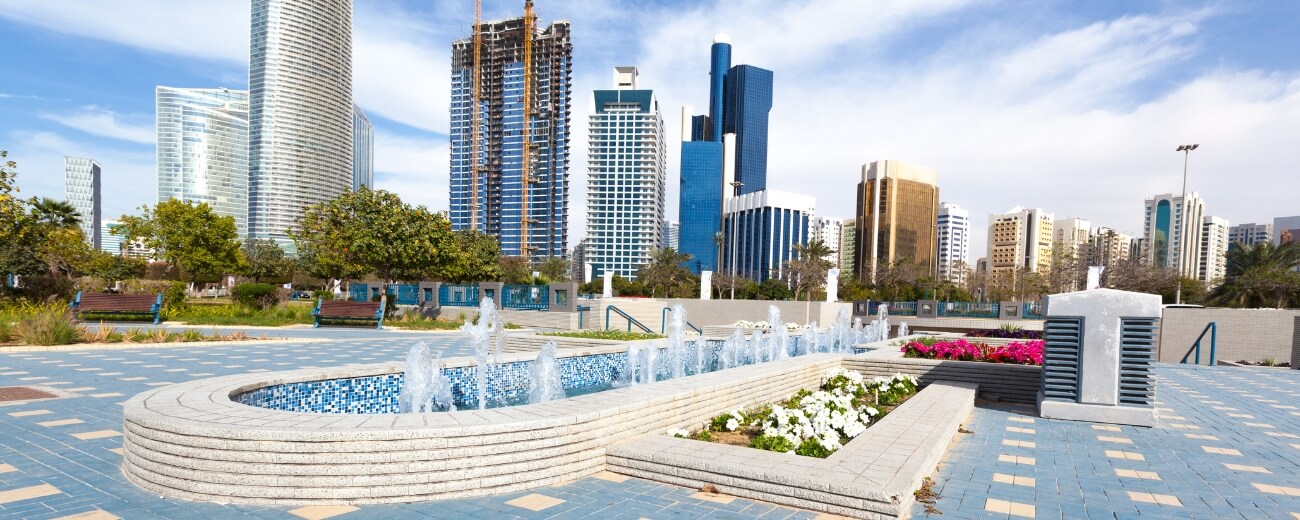 Fountain and flowers in a city park surrounded by modern high-rise buildings in Abu Dhabi