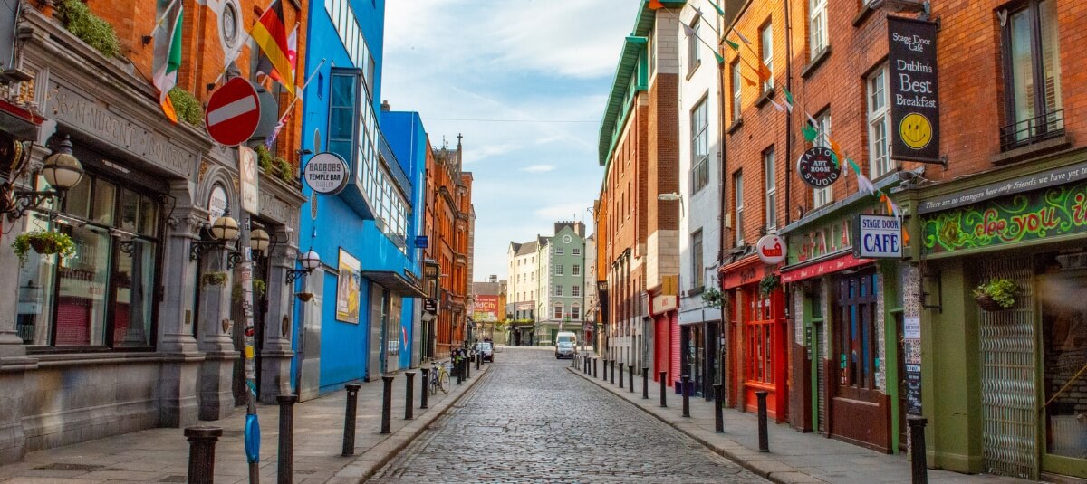 Vibrant Temple Bar street in Dublin with pubs, cafés, and colourful buildings on a cobblestone road.