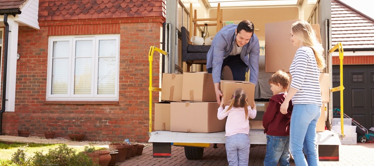 Family with children unloading boxes from a removals van outside their new home after a long-distance move.