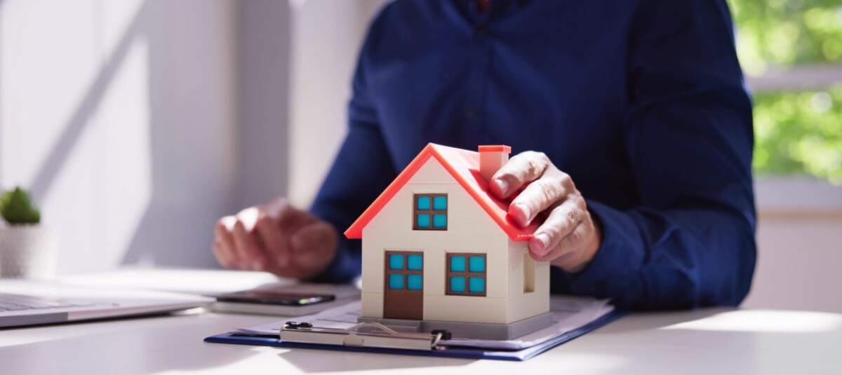 Man reviewing moving costs and home expenses with a model house and clipboard, representing budgeting for a fresh start in a new UK townMan reviewing moving costs and home expenses with a model house and clipboard, representing budgeting for a fresh start in a new UK town