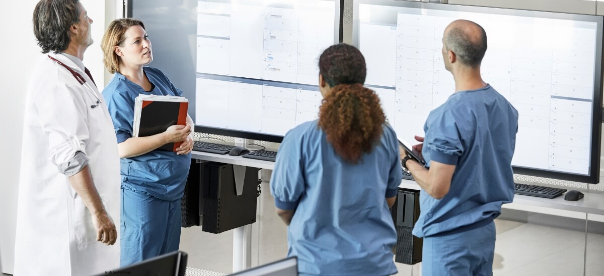 Healthcare professionals in an Irish hospital, including doctors and nurses, discussing patient care using digital screens and technology. Healthcare professionals in an Irish hospital, including doctors and nurses, discussing patient care using digital screens and technology.