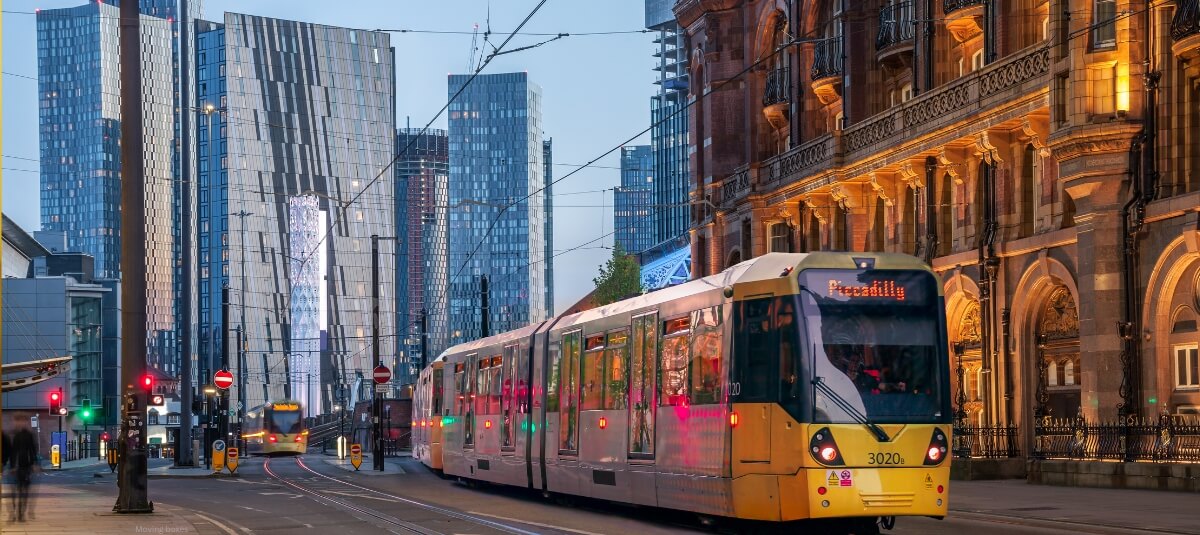 Manchester city centre with tram at Piccadilly, modern skyline and historic buildings at dusk.