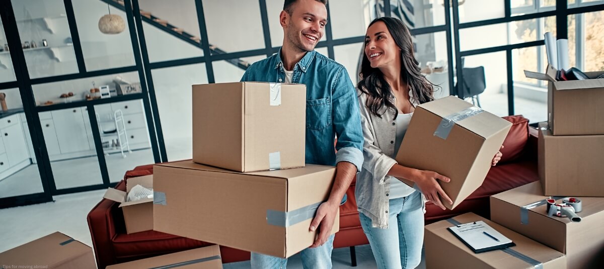 Happy couple carrying moving boxes into their modern new home after relocating abroad Happy couple carrying moving boxes into their modern new home after relocating abroad
