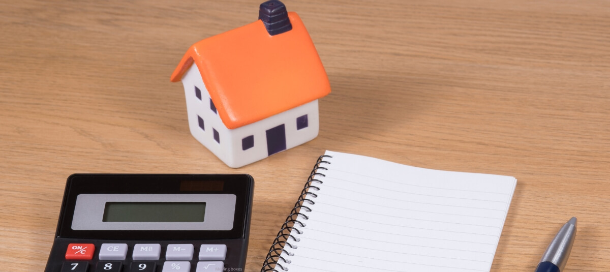 House model with calculator, notebook and pen symbolising the cost planning and budgeting for a house removal.