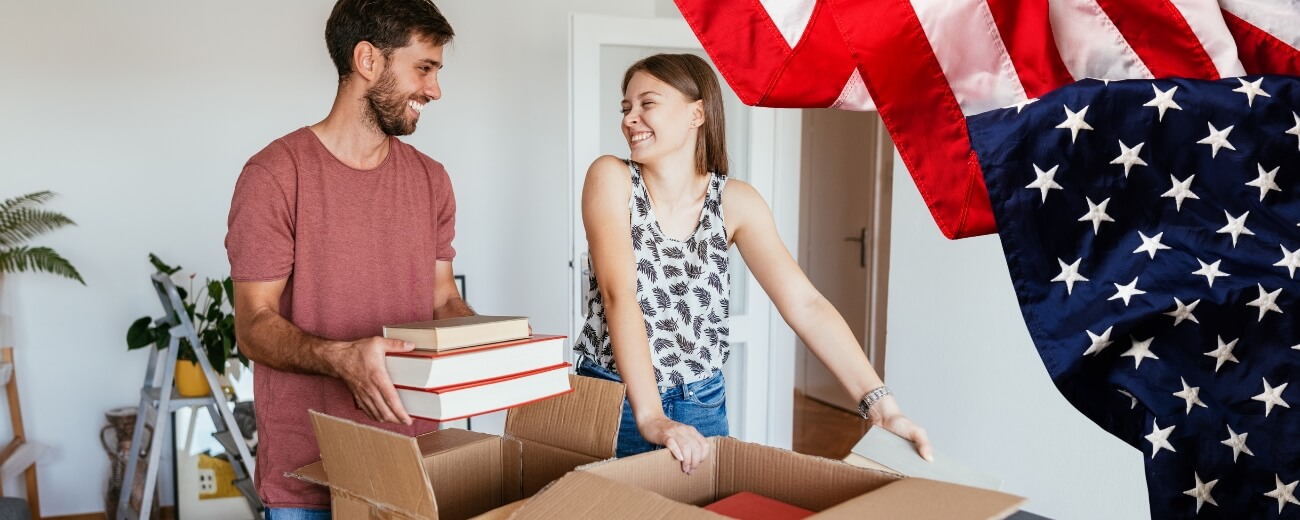 Couple packing boxes for their move from England to America with a large US flag in the background