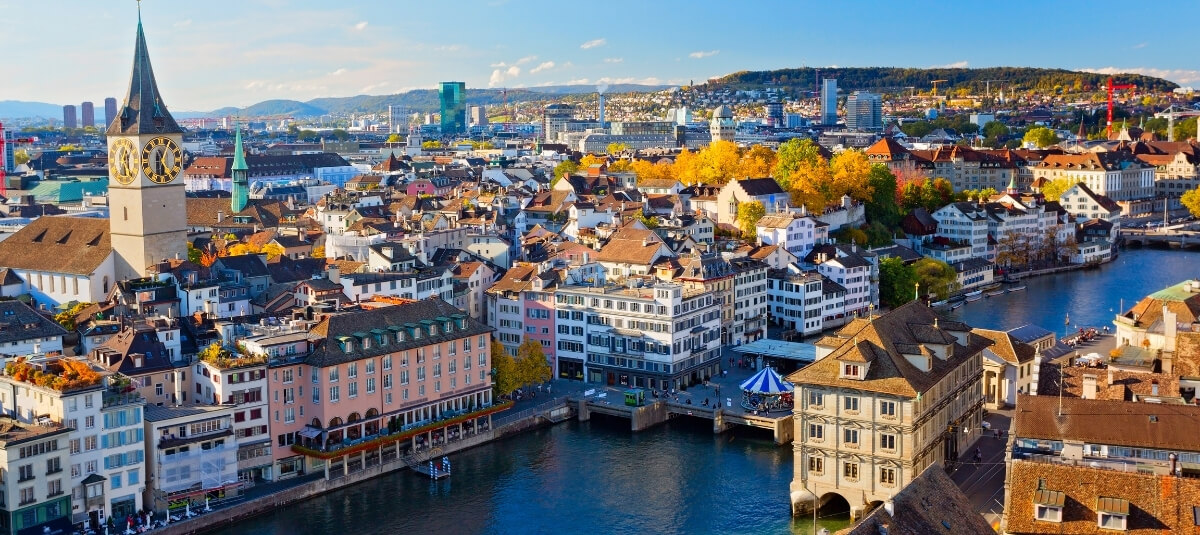 A panoramic view of Zurich city with the Limmat River and Alps in the distance, illustrating the high quality of life for people moving to Switzerland. A panoramic view of Zurich city with the Limmat River and Alps in the distance, illustrating the high quality of life for people moving to Switzerland.