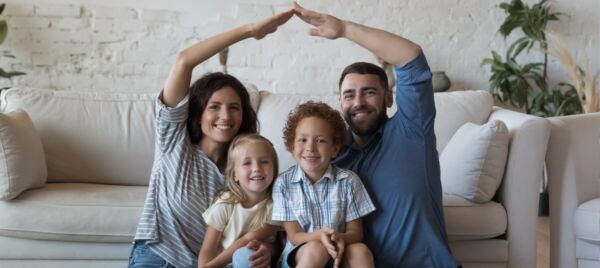 Happy family sitting on a sofa forming a roof shape with their hands, symbolising their new home after moving to the USA from the UK.