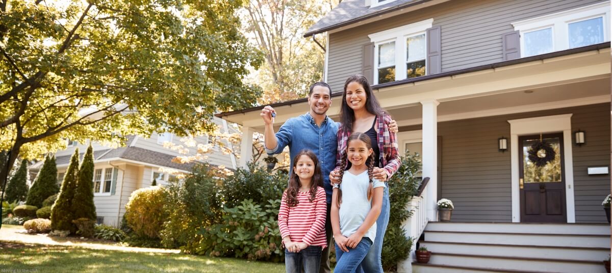 Family holding house keys and standing in front of their new American home, celebrating their successful relocation from the UK to the USA.