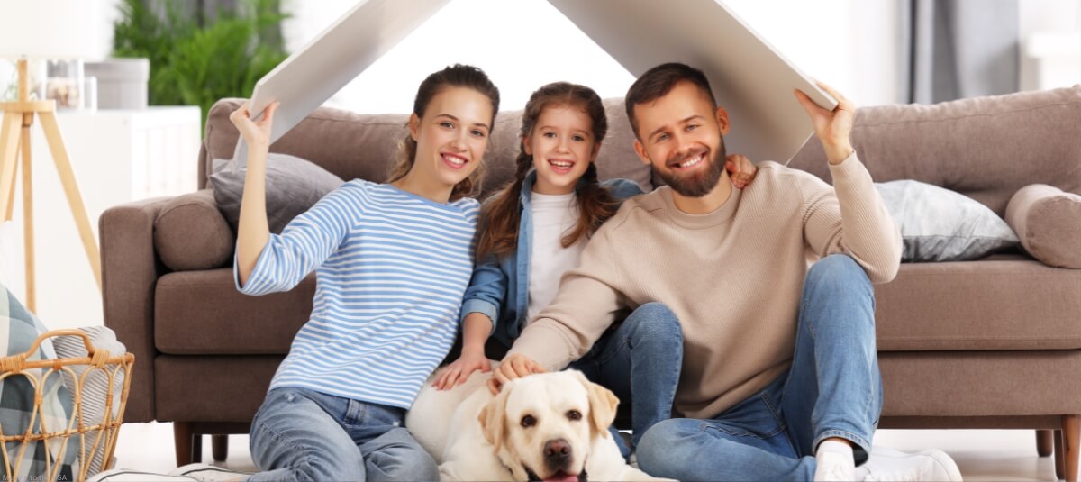 Smiling family with a dog under a roof symbol, representing a pet-friendly home after relocating to the USA from the UK.