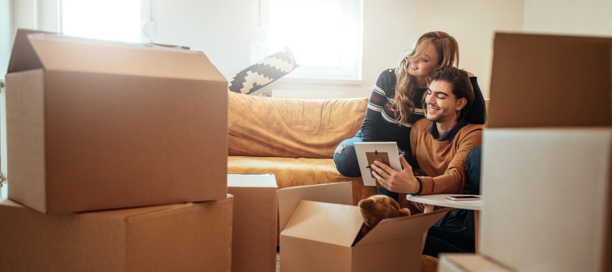 Young couple smiling while unpacking boxes and decorating their new home after moving to a different town in the UK