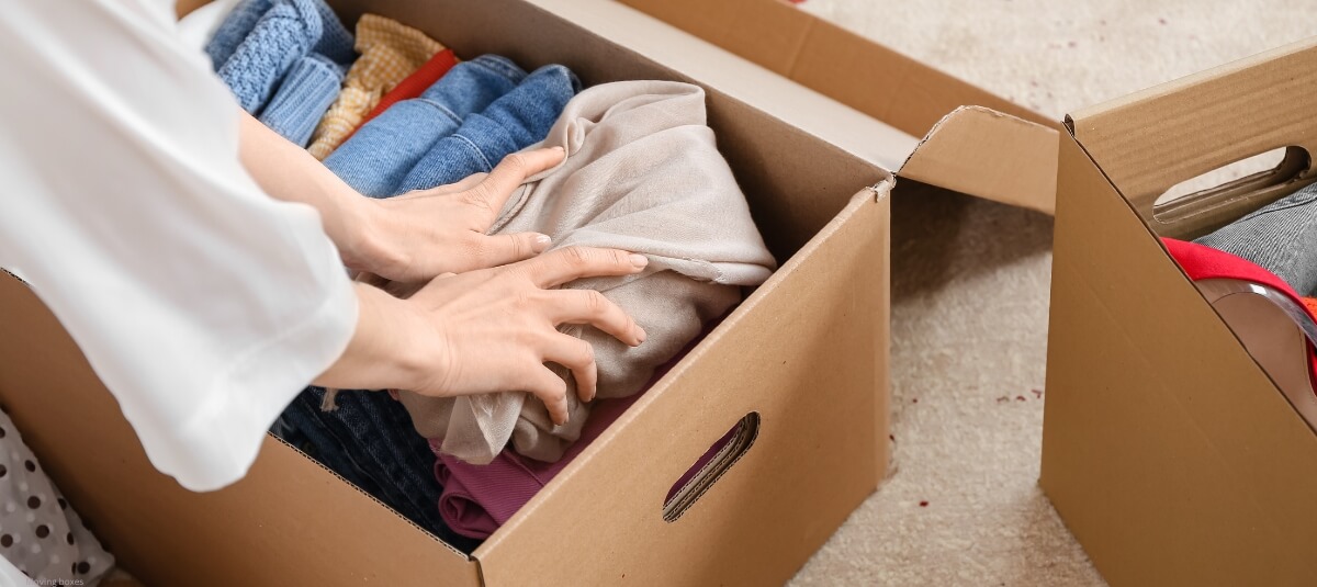 Person packing clothes into a sturdy moving box during house relocation. Person packing clothes into a sturdy moving box during house relocation.