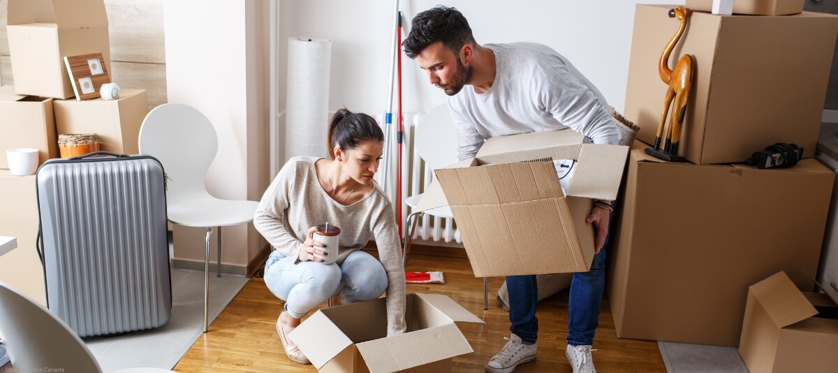 Couple packing boxes in their home, preparing for an international move with a suitcase and moving supplies around them.