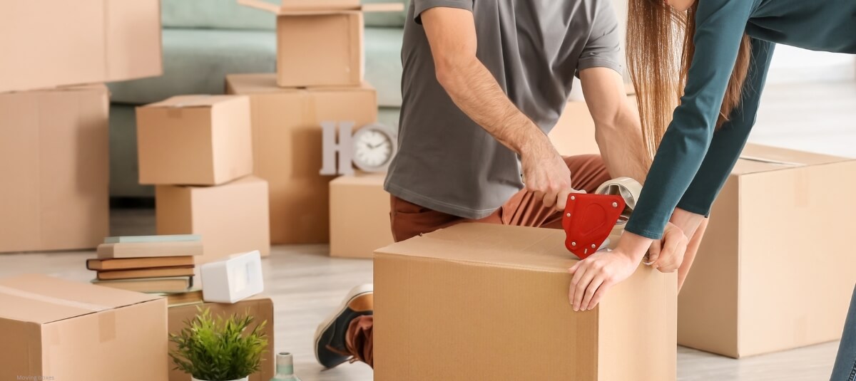 Couple sealing a moving box while preparing for a house move, surrounded by cardboard packing boxes. Couple sealing a moving box while preparing for a house move, surrounded by cardboard packing boxes.