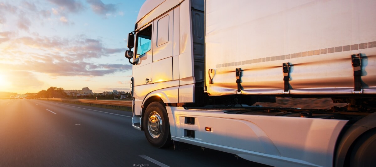 Large removals lorry driving along the motorway during a long-distance move from London to Manchester at sunset.