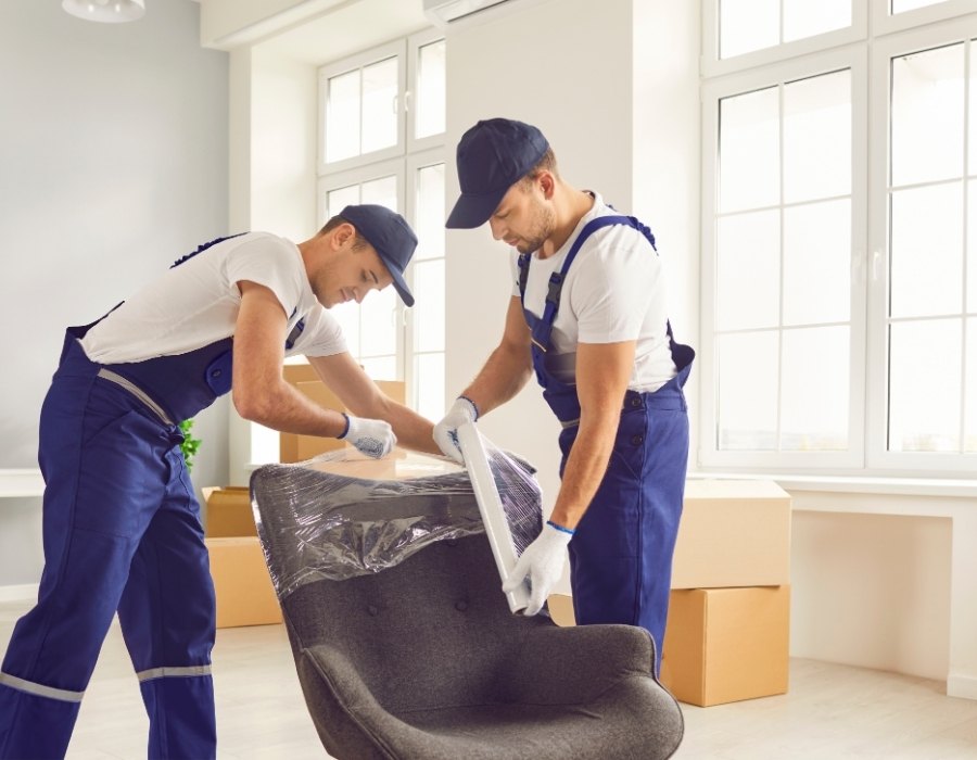 Two removal workers wrapping an armchair in protective plastic before shipping