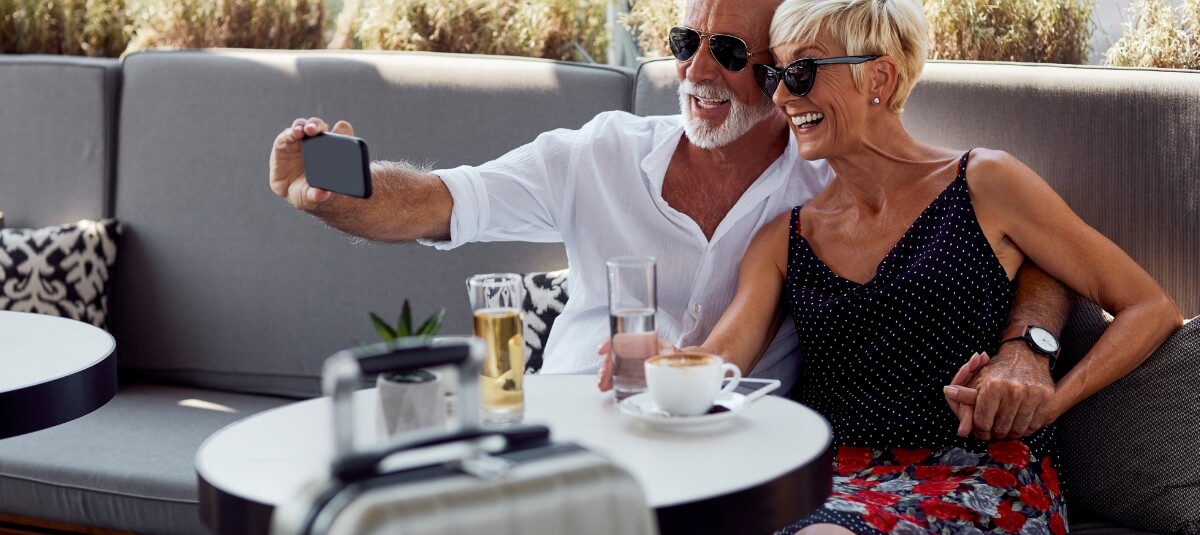 Retired couple from the UK taking a selfie while travelling abroad with coffee and luggage