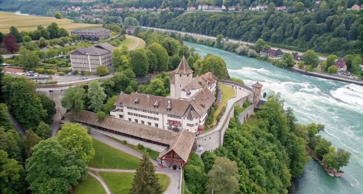 Aerial view of the castle overlooking Rhine Falls near Schaffhausen, surrounded by forest and turquoise river
