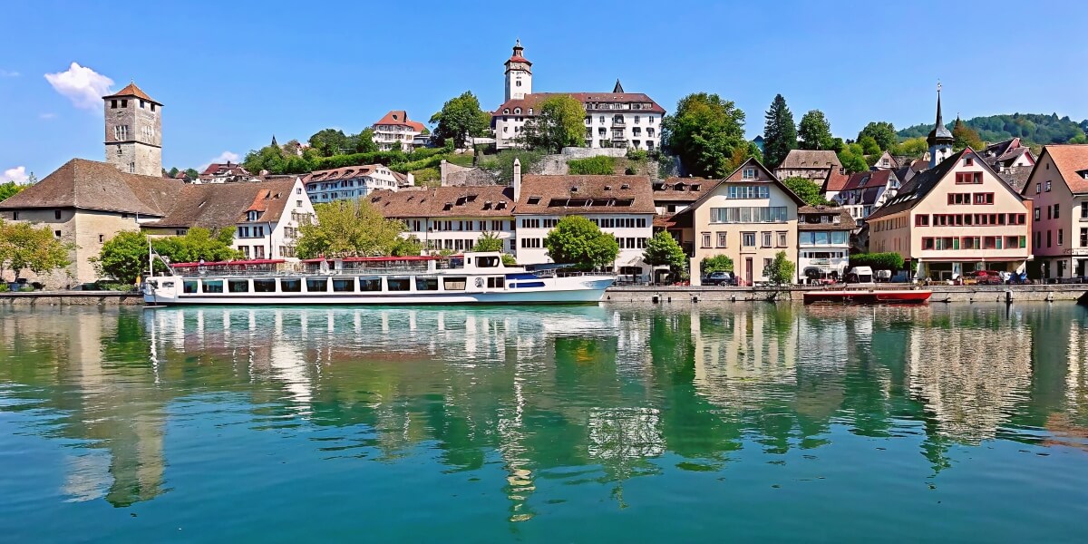 Waterfront view of Schaffhausen with colourful historic buildings and a river cruise boat reflected in the calm Rhine River