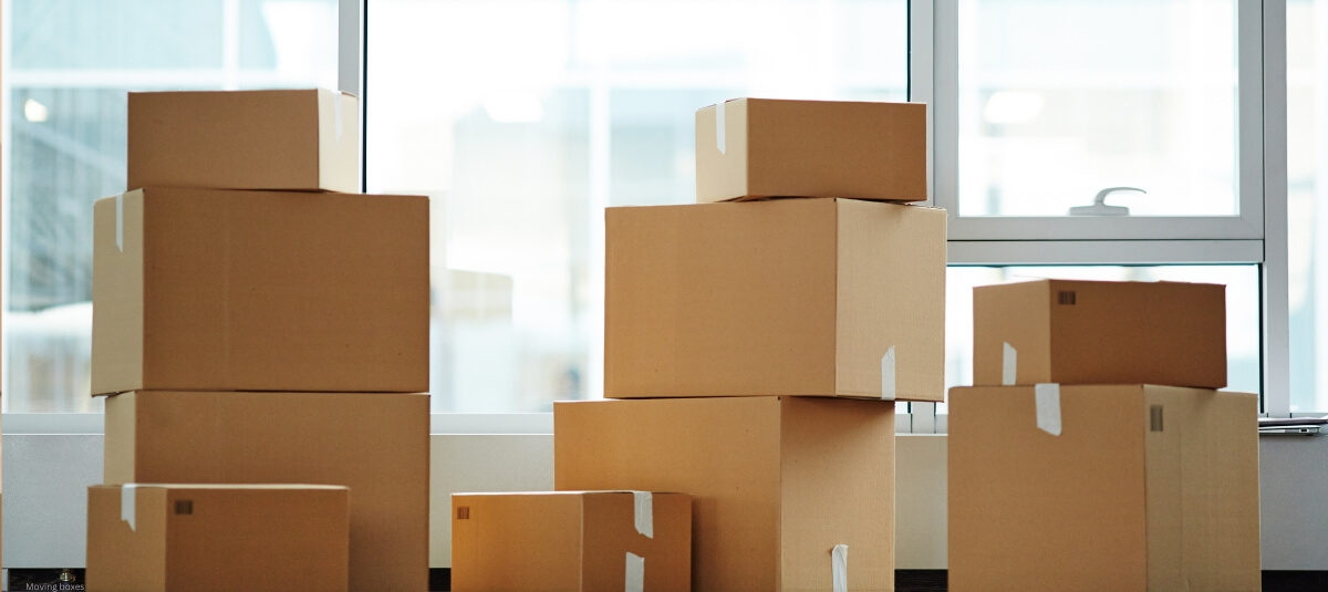 Stack of cardboard moving boxes near a window, ready for house removals or packing. Happy couple carrying moving boxes into their modern new home after relocating abroad