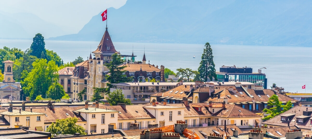 View of a Swiss lakeside city with the national flag, symbolising the country’s strong quality of life and stability for UK residents moving in 2026. View of a Swiss lakeside city with the national flag, symbolising the country’s strong quality of life and stability for UK residents moving in 2026.