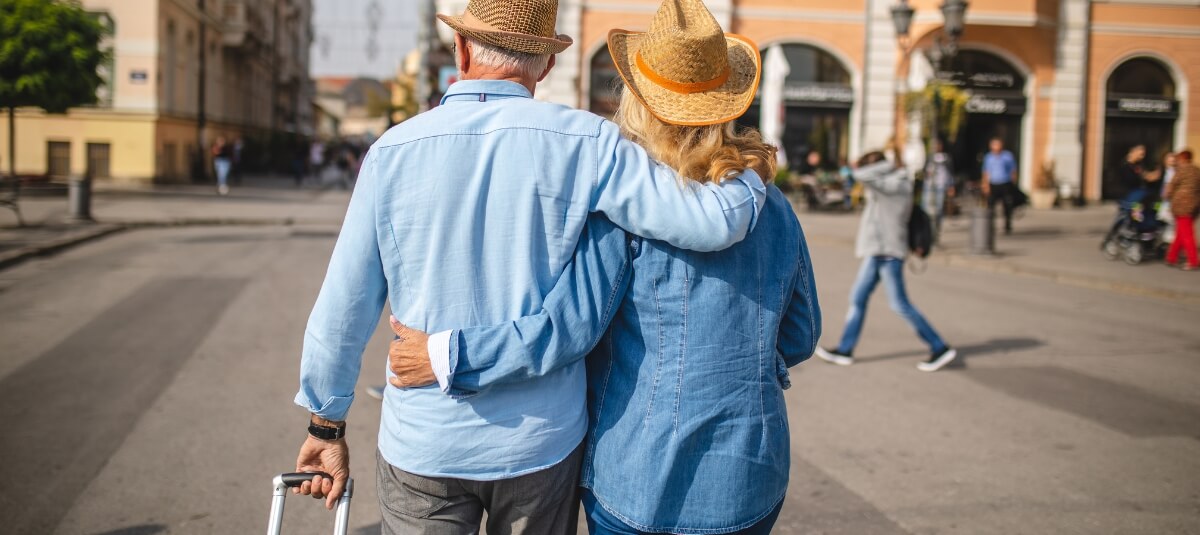 Retired British couple walking with suitcase through a European city after relocating