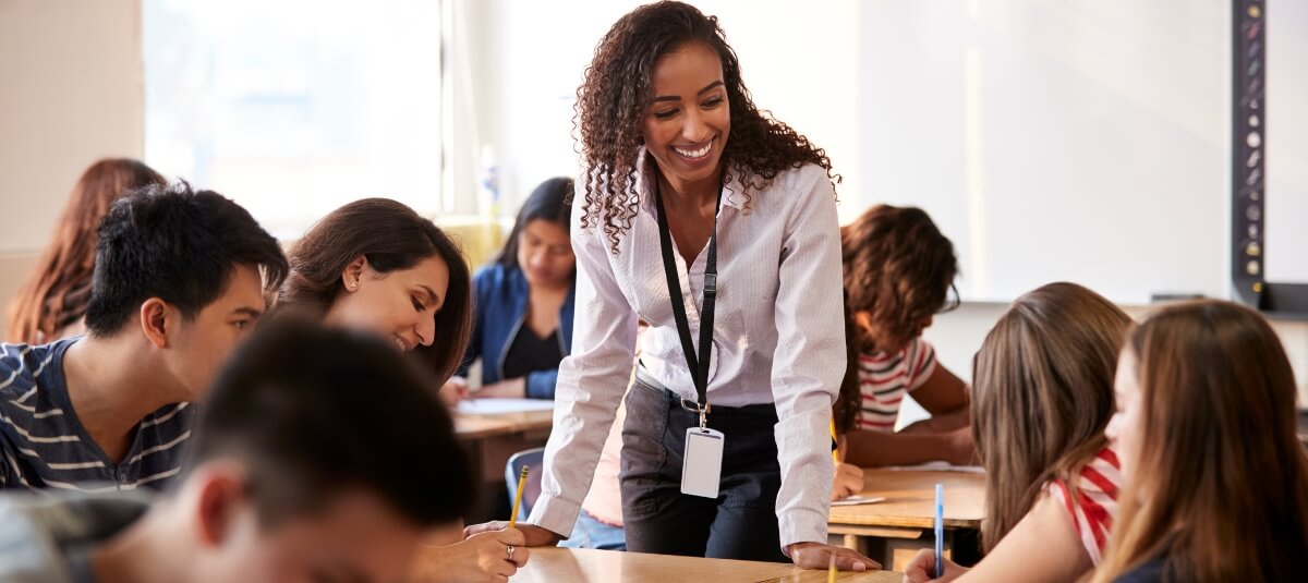 Smiling teacher helping students in a classroom, representing English-speaking job opportunities and teaching roles in France. Smiling teacher helping students in a classroom, representing English-speaking job opportunities and teaching roles in France.